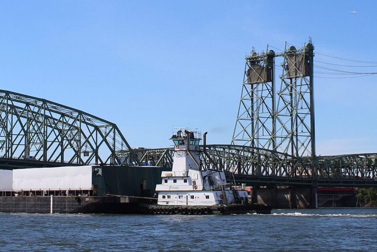 The barge carries the PCCs under a bridge on the Columbia River